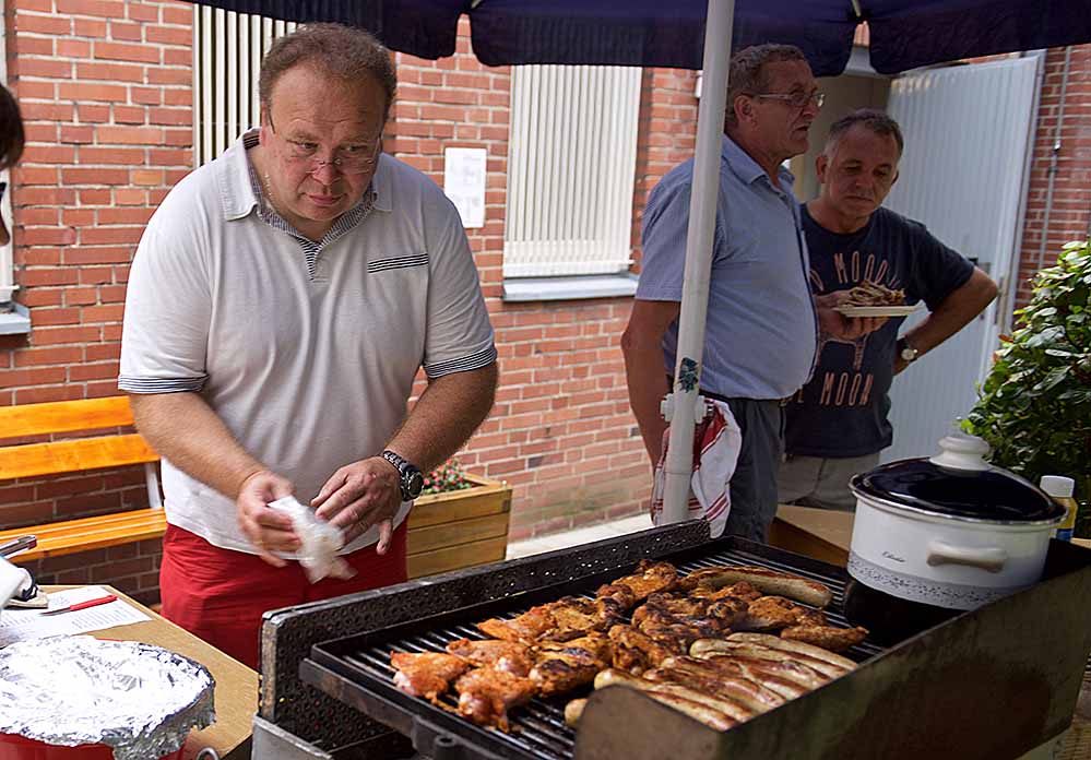 Presbyter Martin Cebulla wendet die Würste und die Hähnchenflügel, die von Küster Georg Geisler (Mitte) bei Metzger Zimmermann kauft.