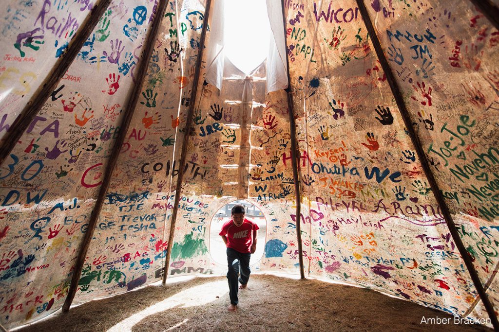 esse Jaso, 12, enters the Unity Teepee, at the Sacred Stone Camp. The teepee is signed by camp supporters from all over North America and around the world. Oceti Sakowin, or the Seven Council Fires, is the true name of the great Sioux nation and refers to the coming together of the different factions of the tribe. Oglala, Cheyenne, Ut, Cree, Hopi and non-indigenous all are among the 200+ tribes represented in the camps and on the front lines. The last time there was a similar gathering was before the Battle of the Little Bighorn, 1876. Story: For nearly 10 months, members of the Standing Rock Sioux tribe and their allies camped out in opposition to the Dakota Access Pipeline crossing their territory and threatening their water supply. The estimated $3.78 billion project, backed by Energy Transfer Partners, is nearly complete, covering almost 1,172 miles. In military vehicles and body armor, police used tear gas, pepper spray, rubber bullets, and water cannons against the protesters, and have been accused of inhumane treatment of arrestees. © Amber Bracken, for Buzzfeed News