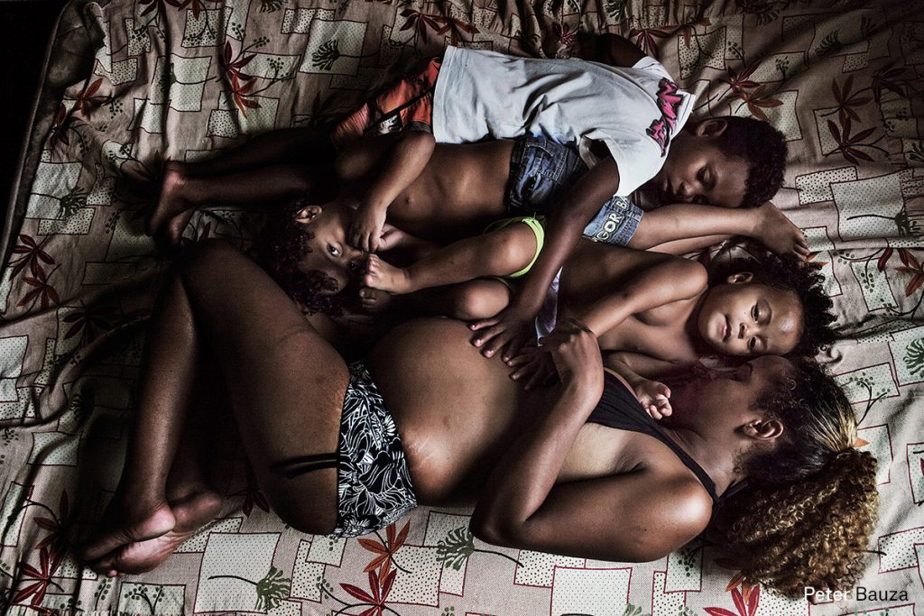 Foto: Peter Bauza Edilane and 3 of her 7 kids (at the time of the shoot) are resting on a mattress on the floor. She is giving soon birth to a son. Despite all her problems and struggling often how to feed her kids next day, she is still positive about her life. Recently she was able to build up a very small and basic Internet store inside the buildings. Out of approx. 10 old computers she makes one for the store. This represents some 5 USD daily. _____ The people of “Copacabana Palace”, also usually called Jambalaya or Carandiru, are the “sem tetos, sem terras”. Generally hidden from view, they represent the dark side of Brazil’s multibillion-dollar spending spree on global sporting events such as the 2007 Pan American Games, the 2014 FIFA World Cup, and the 2016 Olympics. There are thought to be several million people in Brazil without a stable roof (sem moradias), and the number is rising. Despite government housing schemes „minha casa, minha vida“ and anti-poverty policies the “sem tetos, sem terras” (homeless and landless) face a bleak future.