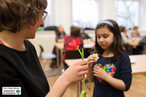 Die Tochter einer Teilnehmerin des Fotoworkshops reicht der Fotografin Sabrina Richmann eine Blume.