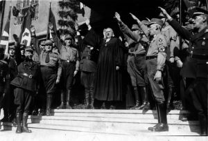 Eröffnung der Nationalsynode in Wittenberg. Landesbischof Ludwig Müller (der spätere Reichsbischof) beim Heilruf mit dem faschistischen Gruß auf Adolf Hitler. 1933 Von Bundesarchiv, Bild 183-H25547 / CC-BY-SA 3.0,