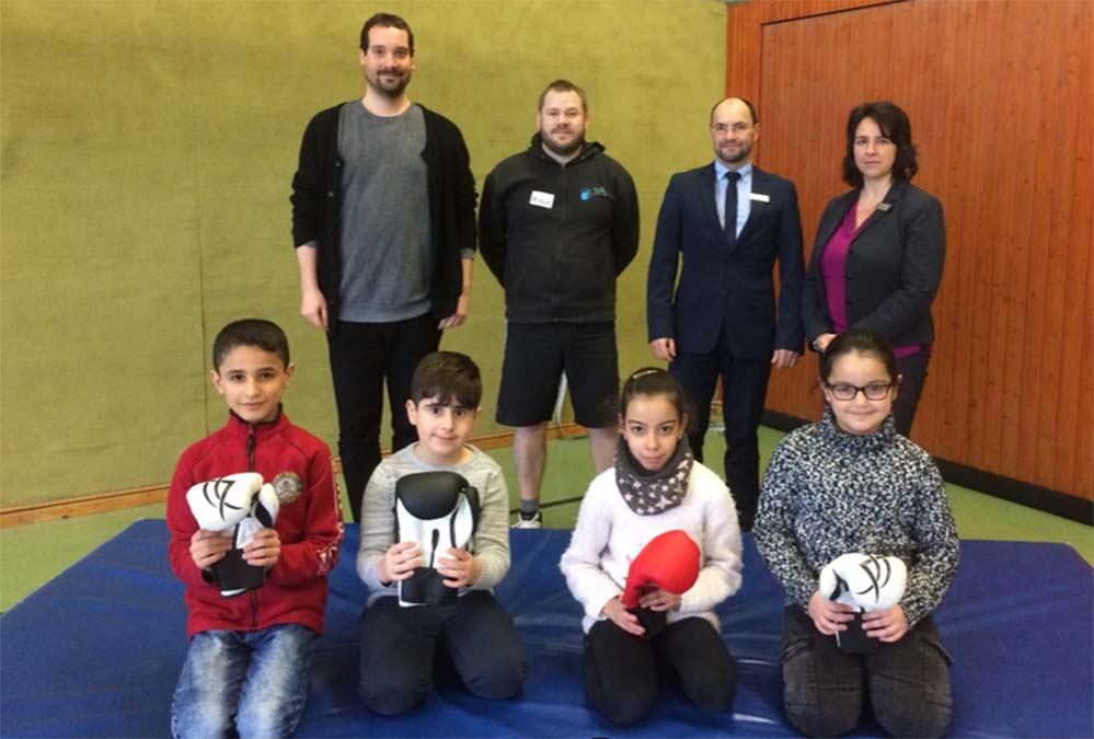 „Respekt-Training“- Sparkasse Dortmund unterstützt Sozialkompetenztraining an der Diesterweg-Grundschule Seit März diesen Jahres wird das Projekt „Respekt-Training“ in der Diesterweg-Grundschule durchgeführt. Der Schwerpunkt des Projekts liegt dabei auf der Selbstkontrolle der Schülerinnen und Schüler sowie auf dem respektvollen Umgang miteinander. Der Pädagoge und Trainer Michael Böhm von der Sozialpädagogischen Initiative Unna e.V. verdeutlicht den Kindern gewaltfreie Konfliktlösungsstrategien, die es in gestressten Situationen im Schulalltag anzuwenden gilt. Dies werde in aktiven Spielen geübt, so Herr Böhm. Bei den Spielen handelt es sich um diverse Kooperationsspiele sowie um sogenannte „Kampfesspiele“, bei denen die Schülerinnen und Schüler auf respektvolle Weise und mit festen Regeln miteinander (und nicht gegeneinander) „kämpfen“ dürfen und ihre Kraft erproben können. Hierbei stehen ganz klar das Miteinander, die wertschätzende Haltung gegenüber allen Beteiligten sowie das individuelle Regelbewusstsein der Teilnehmerinnen und Teilnehmer („innerer Schiedsrichter“) im Vordergrund. Das Respekt-Training wird in allen Klassen des zweiten Jahrgangs der Diesterweg-Grundschule durchgeführt. Ermöglicht wurde das Projekt durch die finanzielle Unterstützung der Stadtsparkasse Dortmund. Foto v.l.n.r.: David Schaffrin (Schulsozialarbeiter der Diesterweg-Grundschule), Michael Böhm (Respekttrainer SPI Unna e.V.), Elmar Steinborn (Leiter Beratungs-Center Sparkasse Münsterstraße), Yvonne Wewers (stellv. Leiterin Beratungs-Center Sparkasse Münsterstraße)