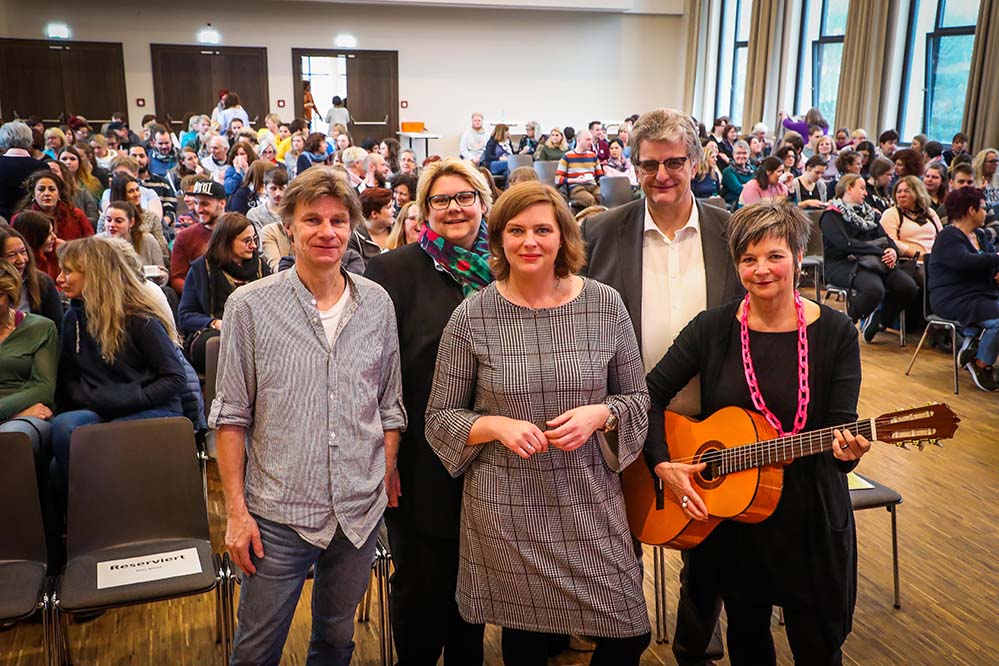 Konflikte meistern Fortbildungstag für 250 Mitarbeitende der Offenen Ganztagsschule Volles Haus im Reinoldinum am Schwanenwall. Eingeladen zu einem Praxistag hatte der Evangelische Kirchenkreis seine Mitarbeitende aus den Offenen Ganztagsschulen (OGS). Gekommen zur Fortbildung waren 250 Pädagoginnen und Pädagogen. Einen „lebendigen und paxisnahen Vortrag“ und einen „wunderbaren Vormittag“ hatten Angela Wolf und Merle Schütte, die Veranstalterinnen, bei der Begrüßung versprochen. Rudi Rohde, Sozialwissenschatler, Schauspieler und Kommunikationstrainer, zeigte in einem informativen, amüsanten und szenischem Vortrag, wie man standhaft und konsequent, aber auch respektvoll und wertschätzend, Konfliktsituationen mit Kindern erfolgreich meistert. Dabei ging es um Stimme und Körpersprache, Deeskalation und konsequentem Handeln. Vor drei Jahren hatte der Kirchenkreis in seinen Offenen Ganztagsschulen eine Umfrage zur Gesundheitsbelastung gestartet. Lärm und hoher Geräuschpegel standen auf der Hitliste ganz weit oben, gefolgt von „der zunehmenden Zahl betreuungsintensiver Kinder“, so Pfarrer Jochen Schade-Homann bei seiner Begrüßung. Schade-Homann ist zuständiger Fachbereichsleiter für die OGS im Kirchenkreis. Die Veranstalter hatten mit dem Thema des Fortbildungstages „Wenn Nervensägen an den Nerven sägen“ folglich ins Schwarze getroffen. 100 leichte Regelverstöße würde es laut einer Umfrage pro Schulstunde geben, so Rohde. Wie reagiert man darauf am besten? Wie begegnet man den Durchsetzungsstrategien von Kindern, die die ganze Klaviatur von Wutanfällen und Schreien bis Leidensmiene und Tränen spielen? „Kinder wollen drei Dinge von uns“, erläuterte Rohde: Wertschätzung, Fairness und Durchsetzungsstärke. „Als OGS-Kraft muss man die ganze Bandbreite drauf haben.“ Der Evangelische Kirchenkreis ist Träger von 32 Offenen Ganztagsschulen. Hier kümmern sich 378 Mitarbeitende um rund 4.000 Kinder. Bildzeile: Der Referent Rudi Rohde zusammen mit Katrin Köster, Merle Schütte, Pfarrer Jochen Schade-Homann und Angela Wolf vom Evangelischen Kirchenkreis. Foto: Stephan Schuetze