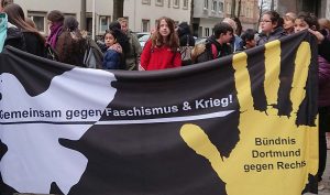 Frühjahrsputz gegen Nazischmutz Ende März gingen 40 SchülerInnen der Heinrich-Böll- Gesamtschule und einige ihrer LehrerInnen gemeinsam mit Mitgliedern des „Bündnis Dortmund gegen Rechts“ und BürgerInnen des Martener Forums in Marten auf die Straße, um rechte Aufkleber aus dem Stadtteil zu entfernen. Am selben Tag begann der Prozess gegen den Martener Neonazi Steven F. Und es jährte sich der Mord an Punker Thomas Schulz („Schmuddel“). Mit Sprühflaschen, in denen eine Spülmittellösung war, und Plastikschabern rückten sie der rechten Propaganda zu Leibe. Dies machte offensicht allen Spaß, wobei sich die SchülerInnen schockiert zeigten, wie viele rechte Aufkleber zu finden waren. Einige AnwohnerInnen fanden offensichtlich auch Gefallen an der Aktion und bedankten sich für die „Säuberung“. Die Polizei war mit mehreren Einsatzwagen vor Ort und auch der Staatsschutz hatte Leute geschickt. Dies war auch nötig, nachdem nach einem ruhigen Anfang der Aktion sieben Neonazis aus Marten und auch aus Dorstfeld begannen, die Gruppe zu „begleiten“, zu filmen, zu fotografieren und auf das Übelste zu beschimpfen. Das Filmen und Fotografieren wurde nicht untersagt, da eine „größere Gruppe von Menschen“ das „Recht am Bild“ verliert. Hier gab es unterschiedliche Reaktionen der TeilnehmerInnen: Die Kleineren fanden das Gebaren der Nazis offensichtlich ein wenig beängstigend, während die älteren SchülerInnen eher offensiver an die „Arbeit“ gingen. Allen Beteiligten war klar, dass dieser Frühjahrsputz ein gutes Zeichen gegen rechte Strukturen im Stadtteil darstellt. Nach einer guten Stunde war die eindrucksvolle Demo zu Ende und die Teilnehmer*innen konnten den Heimweg antreten. Alle sind unbehelligt in der Schule/zu Hause angekommen.