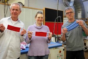 Es halten die Masken hoch: (v. l.) Dr. Klaus Hermansen, Nicole Bugaj und Bernhard Eichhorn, Leiter der Nähwerkstatt, in den Werkstätten der AWO in Dortmund. An der Nähmaschine sitzt Marita Krüger.