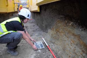 Deutlich erkennbar, die dunkelgrauen Schichten der Grabenverfüllung im Profil und im Planum des Leitungsgrabens. Die Sohle des Wassergrabens wurde bei den Arbeiten nicht erreicht. Denn ausgegraben wird immer nur so viel wie unbedingt durch die Baumaßnahme erforderlich. (Fotos: Stadt Dortmund / LQ-Archäologie