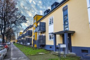 Neue Balkone und frische Farben für  DOGEWO21-Häuser in Dorstfeld   Am Hartweg in Dorstfeld hat DOGEWO21 umfangreiche Instandhaltungs- und Modernisierungsarbeiten abgeschlossen. So erhielten die Häuser Am Hartweg erstmals 1,5x3 Meter große Anstellbalkone. Im Zuge der Maßnahme wurden die Fenster im Balkonbereich erneuert und Balkontüren eingebaut. Die Fassaden der rund 90 Jahre alten Häuser Am Hartweg 139-149 wurden saniert und haben einen freundlichen, neuen Farbanstrich erhalten. Weiter wurden Haustüren und Treppenhausfenster ausgetauscht, Vordächer montiert, die Treppenhäuser gestrichen und mit neuer Elektrik ausgestattet. Für zusätzliche Sicherheit sorgen neue Außenbeleuchtungen sowie Gegensprechanlagen. Die Gesamtkosten für die Maßnahme liegen bei knapp 360.000 Euro.  Die Wiederherstellung der Außenanlagen erfolgt zum Frühjahr 2021.  Nachdem Anfang 2019 bereits die benachbarten Häuser Am Täufling umfangreich saniert und mit Balkonen ausgestattet wurden, wird DOGEWO21 die Instandhaltung der Dorstfelder Siedlung im kommenden Jahr mit weiteren Maßnahmen fortsetzen. Info: Mit über 16.300 Wohnungen zählt DOGEWO21 zu den größten Vermietern in Dortmund. 2020 investiert das Unternehmen insgesamt 34,5 Millionen Euro in Neubauprojekte, Modernisierung und Instandhaltung. DOGEWO21 baut allein in diesem Jahr fast 190 neue Balkone an ihre Häuser in Eving, Huckarde und Dorstfeld an.  Bild: DOGEWO21