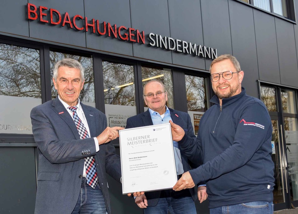 Dachdeckermeister Dirk Sindermann aus Dortmund-Brackel erhält den Silbernen Meisterbrief / Dachdecker-Innung Dortmund und Lünen gratuliert zum Jubiläum / Engagierter Obermeister macht sich stark für die Digitalisierung des Dachdeckerhandwerks. Auf 25 erfolgreiche Jahre als Dachdeckermeister kann der Dortmunder Dirk Sindermann zurückblicken. Anlässlich des Jubiläums kamen jetzt der stellvertretende Obermeister der Dachdecker-Innung Dortmund und Lünen, Jürgen Rohpeter, und Innungsgeschäftsführer Ludgerus Niklas an den Heßlingsweg nach Dortmund-Brackel, um persönlich zu gratulieren. Gemeinsam überreichten sie dem Jubilar eine Ehrenurkunde des Handwerks. „Sie haben mit großer Umsicht und Weitblick nicht nur Ihren eigenen Betrieb aufgebaut, sondern sich auch vorbildlich in der Innung engagiert”, lobte der stellvertretende Obermeister Jürgen Rohpeter. „Darum überbringe ich die herzlichen Glückwünsche aller Innungsbetriebe und überreiche Ihnen Ihren Silbernen Meisterbrief verbunden mit dem Wunsch für weitere fünfundzwanzig erfolgreiche Jahre im Dachdeckerhandwerk.” Leidenschaftlicher Dachdecker Dirk Sindermann hatte im Alter von 16 Jahren seine Lehre im Dachdeckerhandwerk begonnen und darin seinen Traumberuf gefunden. Konsequent bildete sich der leidenschaftliche Handwerker weiter und entschloss sich nach mehreren Jahren als Geselle, seinen Dachdeckermeister zu machen. Er besuchte das Bildungszentrum des westfälischen Dachdeckerhandwerks im sauerländischen Eslohe und legte 1996 erfolgreich die Meisterprüfung vor der Handwerkskammer Arnsberg ab. Zwei Jahre später bestand er auch die Prüfung zum Klempnermeister. 1998 wagte Dirk Sindermann dann zusammen mit einem Kollegen den Schritt in die Selbstständigkeit. Waren es am Anfang noch klassische Dachdeckerarbeiten, die er in seinem jungen Betrieb erledigte, spezialisierte sich Dirk Sindermann mit den Jahren immer weiter. Seit 2006 ist er Gebäudeenergieberater, seit 2008 Fachkraft für die Sanierung von Feuchteschäden und Schimmel und seit 2013 Experte für die Förderprogramme des Bundes. Gleichzeitig wurde er 2013 zum öffentlich bestellten und vereidigten Sachverständigen für das Dachdeckerhandwerk ernannt. Mit den Jahren wuchs auch der Betrieb immer weiter. 2013 wechselte Dirk Sindermann von seinem Gründungsstandort in Deusen nach Dortmund-Brackel in einen Neubau des Unternehmens. Heutiger Arbeitsschwerpunkt des Dachdeckerbetriebs mit 20 Beschäftigten ist neben einer breiten Palette von fachlich hochwertigen Dachdeckerarbeiten vor allem die energetische Gebäudesanierung. Engagement für das Handwerk Ein großes Anliegen war es Dirk Sindermann in all den Jahren stets, sein Handwerk weiter nach vorn zu bringen. Von Anfang an engagierte er sich mit seinem Unternehmen in der Dachdecker-Innung Dortmund und Lünen, wurde 2007 erstmals als Beisitzer in den Vorstand berufen und 2014 zum Obermeister gewählt. Dieses Amt füllt der heute 49-jährige Doppel-Handwerksmeister mit großer Leidenschaft aus, ist seit 2017 auch Vorstandsmitglied im Landesverband des Dachdeckerhandwerks Westfalen und seit 2018 Mitglied im Fachausschuss Metall beim Zentralverband des Deutschen Dachdeckerhandwerks in Köln. Auf Bundesebene treibt Dirk Sindermann vor allem die Umsetzung von Digitalisierungsprozessen im Dachdeckerhandwerk voran und ist selbst Mitglied in einer bundesweiten Arbeitsgruppe, die sich diesem Fachthema widmet. Vor Ort in Dortmund kümmert sich Dirk Sindermann vor allem um den beruflichen Nachwuchs und geht dabei mit gutem Beispiel voran. In seinem Unternehmen wird seit der Gründung ausgebildet und aktuell absolvieren zwei angehende Dachdecker ihre Lehre im Betrieb. Bildzeile: Herzliche Glückwünsche zum Silbernen Meisterbrief mit (v.l.) dem stellvertretenden Obermeister der Dachdecker Innung Dortmund und Lünen Jürgen Rohpeter, Innungsgeschäftsführer Ludgerus Niklas sowie Jubilar und Obermeister Dirk Sindermann. Foto: Dachdecker-Innung Dortmund und Lünen.
