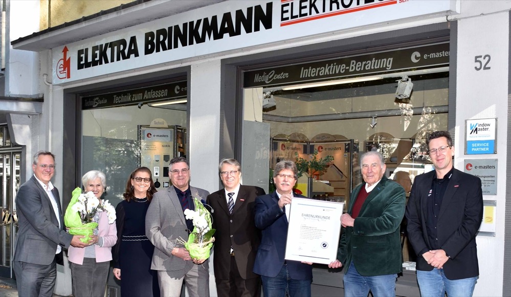 Elektra Brinkmann GmbH & Co. KG an der Märkischen Straße kann auf eine lange Tradition als handwerklicher Fachbetrieb der Elektrotechnik zurückschauen / Vertreter von Kreishandwerkerschaft und Innung gratulieren erfolgreichem Familienbetrieb Ein außergewöhnliches Jubiläum konnte jetzt die Firma Elektra Brinkmann GmbH & Co. KG an der Märkischen Straße in Dortmund feiern. Der Fachbetrieb für Elektrotechnik wurde 90 Jahre alt. Anlässlich des Jubiläums, das wegen der Corona-Pandemie nur im kleinen Kreis gefeiert werden konnte, begrüßten Senior-Chef Udo Beyer und Geschäftsführer Ralf Beyer hochrangige Gäste. Kreishandwerksmeister Dipl.-Ing. Christian Sprenger war zusammen mit dem Obermeister der Innung für Elektrotechnik Dortmund und Lünen, Volker Conradi, und dem Hauptgeschäftsführer der Kreishandwerkerschaft Dortmund und Lünen, Joachim Susewind, an die Märkische Straße gekommen. Sie überreichten anlässlich des Firmengeburtstages eine Ehrenurkunde des Handwerks, verbunden mit den besten Wünschen für die Zukunft des Unternehmens. „Ein Familienbetrieb, wie Sie ihn seit drei Generationen erfolgreich führen, ist eine tragende Säule der Wirtschaft in unserer Region”, so Kreishandwerksmeister Christian Sprenger. „Sie haben mit den Jahren vielen jungen Menschen den Weg in eine sichere Existenz im Handwerk ermöglicht. Unser Handwerk braucht mehr beispielhafte Unternehmer wie Sie und ist Ihnen zu großem Dank verpflichtet. Herzlichen Glückwunsch an Sie, an Ihre Familie und an alle Ihre Beschäftigten.” Ursprünglich für Zechen gearbeitet Die Ursprünge des Familienbetriebs Elektra Brinkmann gehen zurück auf das Jahr 1931. Damals übernahm der Dortmunder Diplom-Ingenieur Otto Baack einen Teil des insolventen Unternehmens „Elektra Jeremias & Herder“, gegründet 1921. Nach dem frühen Tod des Unternehmers 1933 fiel der Betrieb an seine Frau Laura Baack. Diese wiederum heiratete den Dortmunder Elektroinstallateurmeister Erich Brinkmann, der aus der Hinterlassenschaft die Firma „Elektra Brinkmann“ an der Märkischen Straße 66 aufbaute. Sie war mit fast 100 Beschäftigten ursprünglich ein Installationsbetrieb für sieben Dortmunder Zechen und stellte die Betriebselektriker der Schachtanlagen. Nach 1945, als der Betrieb durch Kriegsfolgen zerstört war, zog das Unternehmen zunächst in die Olgastraße 18. 1952 baute Erich Brinkmann dann den heutigen Firmensitz mit Ladenlokal an der Märkischen Straße 52 und legte damit den Grundstein für das heute dort noch ansässige Unternehmen. Der Liebe wegen ins Handwerk Udo Beyer, der heutige Senior-Chef des Unternehmens, kam auf eher ungewöhnliche Weise Anfang der 1960er Jahre in den Betrieb. Der junge Bundeswehroffizier hatte sich in die Tochter des Gründers, Else Brinkmann, verliebt. „Ich wollte eigentlich Brauer werden“, erinnert sich der heute 83-Jährige. „Aber mein angehender Schwiegervater und meine künftige Frau haben mich überzeugt, ins Elektroinstallateurhandwerk einzusteigen.“ So begann Udo Beyer 1962 seine Lehre bei der Firma Wilhelm Ritter in Dortmund und heiratete im April 1964 seine Frau Else Brinkmann. Nach der Lehre absolvierte er 1967 eine Ausbildung zum Techniker und startete gleich in die Meisterausbildung und anschließend in ein Fernstudium der Elektrotechnik zum graduierten Ingenieur. Gerade rechtzeitig, denn nach dem überraschenden Tod von Schwiegervater Erich Brinkmann 1969 musste der junge Meister die Geschäftsleitung übernehmen. Mit den Wandlungen der Stadt gelebt In den 1970er Jahren baut Udo Beyer den Betrieb unter den Vorzeichen des Strukturwandels im Ruhrgebiet um, legt den Schwerpunkt der Arbeit auf Elektroinstallationen am Bau und intensiviert die Zusammenarbeit mit Architekten der Region. 1992 stieg auch sein Sohn Ralf Beyer nach einem Studium zum Diplom-Ingenieur der Versorgungstechnik als zweiter, gleichberechtigter Geschäftsführer in das Unternehmen ein. Er führte den Betrieb in dritter Generation mit sicherer Hand in das Zeitalter der Digitalisierung und ebnete den Weg für einen modernen Fachbetrieb der Gebäudetechnik. Heute deckt das Unternehmen mit 14 Beschäftigten ein breites Spektrum an Leistungen aus dem Bereich der Elektroinstallation und technischen Gebäudeausrüstung ab. Es reicht von der klassischen Installation über die Bereiche von komplexen Smart-Home-Systemen, hochwertigen Video- / Sprechanlagen, Ladeinfrastrukturen zum Laden von Elektrofahrzeugen, Kompetenz im Bereich elektrischer Heizsysteme bis zu sicherheitstechnischen RWA Entrauchungsanlagen. „Als langjähriger Marktpartner der DEW21 stehen ferner unsere Unternehmungen für gemeinsame Nachhaltigkeit mit unterschiedlichen Konzepten im Bereich der aktuellen Energiewende“, so Ralf Beyer. „Aus ökologischer Sicht steigt derzeit auch die Nachfrage nach intelligenten elektrischen Wärmespeicher- und natürlichen Lüftungsanlagen. Letztere tragen durch automatisch betriebene Fenster zur Verbesserung des Raumklimas bei. Eine wesentliche Gesundheitskomponente, die in Zeiten von Corona eine deutliche Gewichtung erfahren hat.“ Großes Engagement im Ehrenamt Besonders hervorgehoben wurde anlässlich des Jubiläumsbesuchs von den Vertretern der Innung und der Kreishandwerkerschaft auch das große ehrenamtliche Engagement des Unternehmens. Schon Firmengründer Erich Brinkmann hatte sich als Innungsmitglied im Handwerk engagiert und war im Meisterprüfungsausschuss der Handwerkskammer aktiv. Udo Beyer setzte dieses Engagement sowohl mit seinem Innungsbetrieb, als auch persönlich fort. Von 2000 bis 2009 war er Obermeister der Innung für Elektrotechnik Dortmund und Lünen, gleichzeitig Delegierter der Kreishandwerkerschaft Dortmund und Lünen und Delegierter des Fachverbandes Elektro- und Informationstechnische Handwerke NRW. Aufgrund seiner Verdienste wurde er von der Innung 2009 zum Ehrenobermeister ernannt. Sein Sohn Ralf Beyer tritt in die Fußstapfen seines Vaters. Er war ab 1996 zunächst drei Jahre Kassenprüfer der Innung, ab 2004 Delegierter des Fachverbands und ist seit 2009 Mitglied des Innungsvorstands. Hier ist er seit 2014 stellvertretender Obermeister der Innung und Delegierter der Kreishandwerkerschaft. Über die Jahre war „Elektra Brinkmann” darüber hinaus immer auch um die Ausbildung des beruflichen Nachwuchses bemüht. Mehr als 250 Auszubildende fanden in den 90 Jahren des Bestehens über die Firma den Weg in das Elektrotechnikerhandwerk. Einige haben sogar den Weg bis zum Meister geschafft. Auch für die nächsten Jahre hat das Unternehmen bereits vorgesorgt: Elektromeister und Betriebsleiter André Grandau, der selbst bei „Elektra Brinkmann“ vor 28 Jahren in die Lehre ging, wird das alteingesessene Unternehmen in die nächste Generation überführen. Bildzeile: Feierliche Überreichung der Ehrenurkunde des Handwerks zum Jubiläum mit (v.l.) Geschäftsführer der Innung für Elektrotechnik Dortmund und Lünen Joachim Susewind, Else Beyer, Birgit Beyer und Geschäftsführer Ralf Beyer (stv. Obermeister der Innung für Elektrotechnik Dortmund und Lünen), Kreishandwerksmeister Christian Sprenger, Obermeister der Innung für Elektrotechnik Dortmund und Lünen Volker Conradi; Senior-Chef Udo Beyer und Betriebsleiter André Grandau.