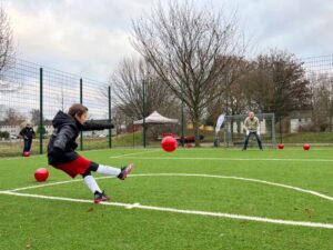 Endlich ist es soweit! Der Bolzplatz am Spielplatz Im Odemsloh in Westerfilde & Bodelschwingh ist fertig. Die Kids können sich ab sofort über ein neues Kunstrasen-Kleinfeld zum Fußballspielen und einen Kunststoffplatz zum Ballspielen (u.a. Basketball) freuen. Gemeinsam mit der E1-Jugend von Rot Weiß Germania, dem Bezirksbürgermeister Axel Kunstmann, dem Büro für Kinder- und Jugendinteressen des Jugendamtes, dem Grünflächenamt, dem Amt für Stadterneuerung und dem Quartiersmanagement Westerfilde & Bodelschwingh wurde der Multifunktionsplatz jetzt eingeweiht. Der Bezirksbürgermeister begab sich ins „Duell“ mit den junge*n Schütz*innen von Rot-Weiß Germania und stellte sich für ein Elfmeterschießen ins Tor. Bei milderen Temperaturen folgt im Frühjahr 2022 die Linierung des Kunststofffeldes und im Anschluss eine Ball-Olympiade für alle Kinder und Jugendlichen aus Westerfilde & Bodelschwingh. Der Neubau des Multifunktionsplatzes ist die erste Maßnahme aus dem Spielraum- und Freizeitflächenkonzept für Westerfilde & Bodelschwingh, die umgesetzt wird. Der Platz wurde im Rahmen des Programms „Soziale Stadt Westerfilde & Bodelschwingh“ unter der Federführung des Amtes für Stadterneuerung umgebaut, in dem unterstützt durch Fördermittel des Landes und des Bundes unterschiedliche Maßnahmen zur Stärkung des Quartiers durchgeführt werden. Ein Schwerpunkt des Programms ist die Umsetzung des Spielraum- und Freizeitflächenkonzeptes mit einer Vielzahl von Maßnahmen für verschiedene Zielgruppen. So soll unter anderem auch der Spielplatz „Im Odemsloh“, in den der Multifunktionsplatz eingebettet ist, in den nächsten Jahren aufgewertet und zu einem attraktiven Spielplatz mit Aufenthaltsflächen für unterschiedliche Alters- und Bevölkerungsgruppen werden. Hierzu wurden vom Quartiersmanagement bereits im Sommer Anregungen und Wünsche aus den Stadtteilen Westerfilde & Bodelschwingh gesammelt. Die Ideen sind die Grundlage für die weitere Planung, die in Abstimmung zwischen dem Jugendamt, Büro für Kinder- und Jugendinteressen, und dem Grünflächenamt in den nächsten Monaten erfolgt. Auf die Neugestaltung des restlichen Spielplatzes darf man also gespannt sein.