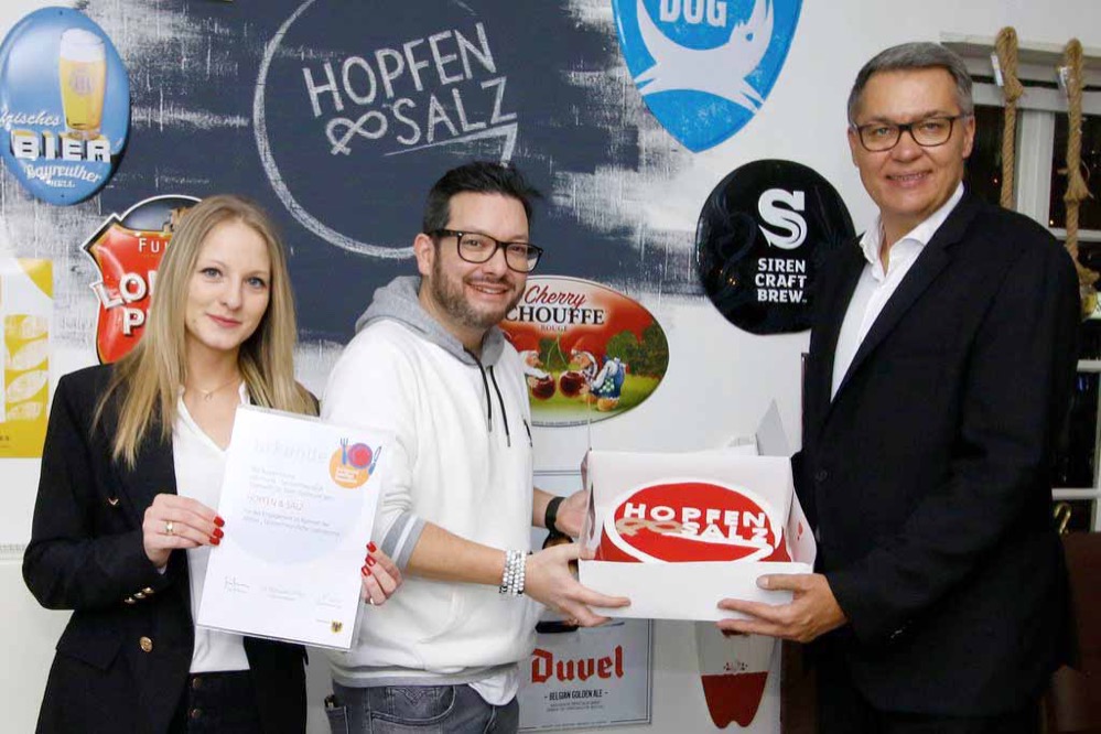 Das Restaurant „Hopfen und Salz“ in Lütgendortmund ist nun offiziell eine familienfreundliche Gastronomie: Heute (Mittwoch) verlieh Oberbürgermeister Thomas Westphal dem Gastronomiebetrieb an der Volksgartenstraße 61 die Auszeichnung „Dortmund – familienfreundlich“. Seit Ende 2008 unterstützt das Dortmunder Jugendamt mit diesem Service Familien bei der Suche nach einem geeigneten Restaurant. Neben der Auszeichnung überreichte Oberbürgermeister Thomas Westphal dem Geschäftsführer Antonio Link und seiner Frau Martha auch einige Exemplare des Plappermaul-Malbuchs, das 18 Erlebnisorte in Dortmund für Kinder und Familien vorstellt, sowie Vorlese- und Lesebücher aus der Plappermaul-Reihe zum Vorlesen und Selberlesen. Sie ergänzen nun das kindgerechte Angebot im Restaurant. Die als familienfreundlich bewerteten Betriebe sind im Familien-Portal auf der Internetseite der Stadt Dortmund unter dortmund.de/familie unter dem Menüpunkt „Angebote für junge Familien“ zu finden. Die Bewertung nehmen die Betriebe anhand einer Checkliste selbst vor. Kriterien für die Auszeichnung als familienfreundlicher Betrieb sind „Service und Angebote für Kinder“, „Preis-/Leistungsverhältnis“ und „Ausstattung/Einrichtung im Innenbereich“ mit jeweils neun Unterkriterien: Gibt es einen barrierefreien Zugang, Familientische, Kinderhochstühle und einen Abstellbereich für Kinderwagen? Sind Kinderbesteck oder ein eigener Spielbereich vorhanden? Gibt es kleinere, reduzierte Kinderportionen und Rohkost mit Dip anstelle von Salat? Betriebe, die nach eigener Einschätzung jeweils drei der Unterpunkte pro Hauptbereich erfüllen, erhalten die Auszeichnung und werden ins Familien-Portal aufgenommen. Die detaillierte Checkliste der Präventionsfachstelle im Jugendamt und der DEHOGA Westfalen e.V. deckt verschiedenste Anforderungen und Möglichkeiten einer als familienfreundlich einzustufenden Gastronomie ab. Interessierte Gastronom*innen sind auch weiterhin zur Beteiligung an der Aktion eingeladen. Den Bewerbungsbogen gibt es als Download im Familien-Portal. www.dortmund.de/familie Auf dem Foto OB Thomas Westphal mit „Hopfen und Salz“-Geschäftsführer Antonio Link und seine Frau Martha.
