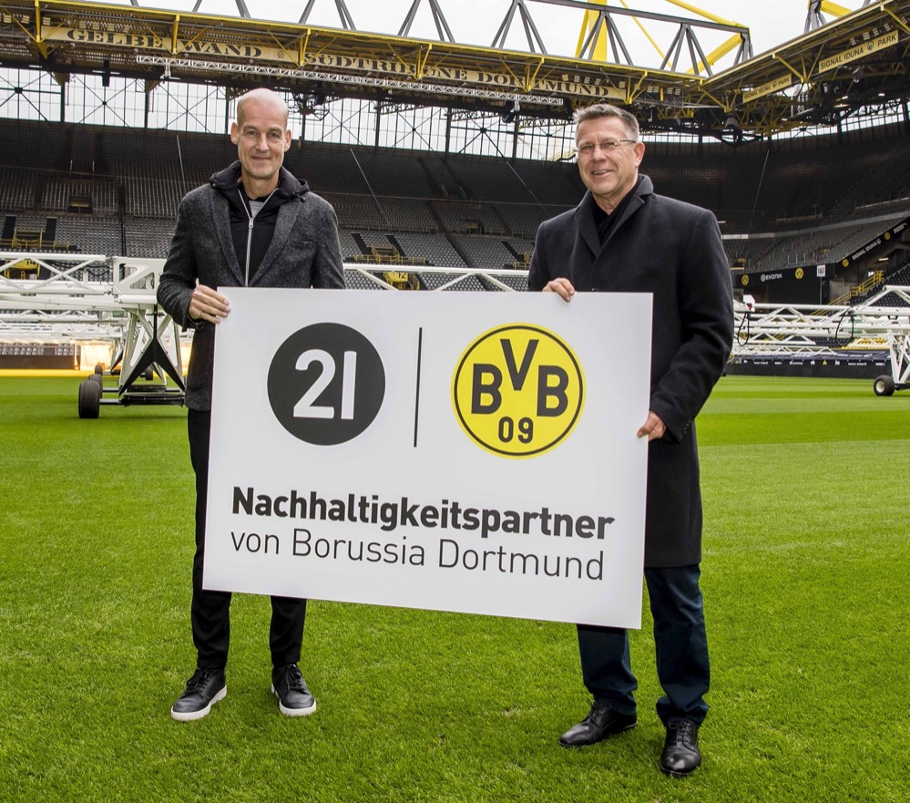 Manchmal sind zwei Partner einfach füreinander geschaffen. Auf den BVB und die Dortmunder Stadtwerke AG – DSW21 trifft das unstrittig zu. Dass die beiden Platzhirsche ihre faktisch seit Jahrzehnten und vertraglich seit Beginn des DSW-Markenjahres 2021 bestehende Zusammenarbeit mit dem Schwerpunktthema „Nachhaltigkeit“ nun bis Ende der Saison 2023/24 verlängern, ist da irgendwie nur logisch. Guntram Pehlke, Vorstandsvorsitzender von DSW21, und BVB-Geschäftsführer Carsten Cramer besiegelten jetzt die Fortsetzung. „Die Partnerschaft hat uns im Jahr der Familienmarke 21 eine hohe Sichtbarkeit verschafft, mit der wir auch in Zukunft viele gemeinsame Ziele miteinander erreichen können“, sagt Guntram Pehlke. „Umweltschutz, Nachhaltigkeit, Chancengleichheit, gesellschaftliches Engagement, kurz: ein noch besseres Dortmund für alle - das ist und bleibt eine Teamaufgabe, die wir gerne gemeinsam mit dem BVB angehen.“ Auch Carsten Cramer freut sich über die Fortsetzung der Kooperation: „Die 21 ist mehr als eine symbolische Rückennummer auf einem unserer Trikots. Als Unternehmensverbund der Daseinsvorsorge ist sie aus Dortmund genau so wenig wegzudenken wie der BVB. Die Verlängerung der Partnerschaft werden wir nutzen, um unseren Heimvorteil gemeinsam auszuspielen.“ Der Traditionsverein und das Traditionsunternehmen arbeiten de facto seit vielen Jahren auf unterschiedlichen Feldern eng zusammen. So befördert DSW21 – jedenfalls in Nicht-Coronazeiten – mit Bussen und Stadtbahnen an jedem einzelnen Heimspieltag zwischen 30.000 und 35.000 Fans zum Signal Iduna Park und wieder nach Hause. Das spart pro Saison, wenn man Bundesliga, DFB- und Europapokal aufaddiert, mehr als 3.000 Tonnen CO2. Zudem hat DSW21 als Investor und Bauherr vom ersten Spatenstich an das Trainingsgelände und Leistungszentrum des BVB in Brackel entwickelt, an Borussia vermietet und inzwischen in Teilen an den Klub übergeben. Zuletzt wurde im Sommer 2020 die Geschäftsstelle Sport fertiggestellt. Hintergrund dieser Zusammenarbeit: Als die Schwarzgelben 2005 auf dem Höhepunkt der Finanzkrise ein Nachwuchsleistungszentrum errichten mussten, um die Lizenz zu erhalten, stemmten die Stadtwerke das Invest. DSW21-Immobilienchefin Silke Seidel, federführend bei der Entwicklung in Brackel, sprang in diesem Jahr auch als Projektleiterin ein, als es beim Umbau des BVB-Museums „Borusseum“ hakte. Das Ergebnis: In Kürze ist endlich Wiedereröffnung. Die Liste der erfolgreichen gemeinsamen Projekte lässt sich fortsetzen: So fuhr der Corona-Testbus von DSW21 von Frühjahr bis Herbst 2021 auch die Betriebsstandorte des BVB an, damit dessen Beschäftigte sich direkt am Arbeitsplatz testen lassen konnten. Das Dortmunder Verkehrsunternehmen verlieh der schwarzgelben Stadtbahn anlässlich des zehnjährigen Jubiläums eine komplett neue Beklebung und brachte mit der BVB-Legendenbahn im Rahmen der Kampagne für die Familienmarke 21 ein zweites Fahrzeug ins Liniennetz. Der gemeinsam gebrandete Airport-Tower ist seit Februar ein echter Markenleuchtturm am östlichen Stadteingang. Und schließlich ist die kommunale Unternehmensgruppe von Tag eins an Partner der neuen Frauenfußball-Ära beim BVB. Als solcher präsentiert die 21 seit Saisonbeginn die Übertragungen der Heimspiele des Frauen-Teams auf Borussias Twitch-Kanal. Aber auch beim gesellschaftlichen Engagement gehen die Partner Hand in Hand. So spendete DSW21 in diesem Jahr eine Summe von 25.000 Euro für die BVB-Stiftung „leuchte auf!“, während Carsten Cramer als Jurymitglied beim DSW21-Förderwettbewerb #dortMUT mitwirkt. In dessen Rahmen unterstützen die Stadtwerke Projekte von Vereinen und gemeinnützigen Organisationen jedes Jahr mit 84.000 Euro. Im kommenden Frühjahr starten beide dann gemeinsam mit weiteren Dortmunder Partnern ein Azubi-Projekt gegen Rassismus und Antisemitismus. „Das alles beweist eindrucksvoll, dass unsere Zusammenarbeit nicht nur auf dem Papier besteht, sondern im Alltag gelebt wird“, so Guntram Pehlke und Carsten Cramer. Manchmal sind zwei Partner einfach füreinander geschaffen … FOTO: BVB-Geschäftsführer Carsten Cramer und Guntram Pehlke, Vorstandsvorsitzender von DSW21, besiegeln die Fortsetzung der Nachhaltigkeitspartnerschaft bis Ende der Saison 2023/24.
