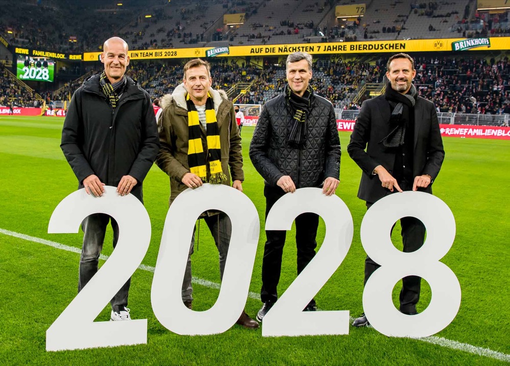 Auf dem Foto: (v.l.n.r): BVB-Marketingchef Carsten Cramer, Uwe Helmich und Thomas Schneider (beide Brauerei-Geschäftsführer) sowie Thomas Joos, Executive Director SPORTFIVE Germany GmbH c/o Borussia freuen sich auf die verlängerte Partnerschaft zwischen Borussia Dortmund und Brinkhoff’s bis 2028. „Echte Liebe“ ist es, was diesen Verein und sein Bier verbindet: Seit dem Jahr 2008 sind Borussia Dortmund und Brinkhoff’s gemeinsam am Ball. Und das soll auch so bleiben! Die Partnerschaft soll langfristig fortgesetzt werden, bis mindestens zum Saisonende 2028. Damit steht schon heute fest: Die Schwarzgelben und das Bier aus dem Revier werden dann ihre 20-jährige Zusammenarbeit feiern können. Alles außer gewöhnlich Alles bleibt? Wie gewohnt? Und damit erwartbar? Im Gegenteil: In diesen schnelllebigen Zeiten ist es durchaus etwas Besonderes, was Borussia Dortmund und Brinkhoff’s verkünden können. Denn welches Unternehmen, welche Marke bindet sich heute noch so frühzeitig und vor allem so langfristig an einen Partner? „Eine so lange, konstante und vertrauensvolle Partnerschaft, wissen wir zu schätzen und wir freuen uns sehr auf das zukünftige Miteinander. Wir werden weiterhin alles dafür tun, dass wir diese Erfolgsgeschichte fortschreiben können“, so BVB-Marketingchef Carsten Cramer. Pure Emotionen Dem kann sich Uwe Helmich nur anschließen: „Die Schwarzgelben waren und sind eine Herzensangelegenheit. ‚Echte Liebe‘ ist für uns eben keine Worthülse, kein leeres Versprechen, im Gegenteil“, so der Brauerei-Geschäftsführer. „Wir jubeln, lachen, feiern und leiden gemeinsam. Das ist Emotion pur! Vor allem aber sind wir beide auch unglaublich stolz auf unser Revier, ticken im selben Takt, und das spüren die Fans – übrigens weit über die Fußball- und Bierstadt Dortmund hinaus.“ Neue Spielfelder Getragen von dieser Fan-Liebe haben die Brauerei-Verantwortlichen seit dem Beginn der Partnerschaft im Jahr 2008 zudem stetig neue Spielfelder besetzt, um ihren Verein auch jenseits des heimischen Epizentrums zu unterstützen. „Die Fußball-Talkshow ‚Brinkhoff’s Ballgeflüster‘ beispielsweise, bei der wir schon unglaublich spannende Gäste und wahre Gänsehaut-Momente erlebt haben. Oder unsere begehrten BVB-Sondereditionen, die zu Sammlerstücken geworden sind. Damit machen wir weiter, und wir haben da schon ein paar richtig gute Ideen“, deutet Geschäftsführerkollege Thomas Schneider an.   Die einzigartige Fan-Kultur rund um Borussia Dortmund ist die Brauerei schon lange ein echtes Anliegen: So ist sie schon seit fast zwei Jahrzehnten Partner des Fan-Projekts Dortmund e.V. – und damit hier schon deutlich länger am Ball als bei den Fußball-Profis. Auch dieses langjährige Miteinander geht in die Fortsetzung. Ganz neu ist hingegen, dass Brinkhoff’s das BVB-Engagement mit weiteren Partnerschaften vertieft: Seit dieser Saison unterstützt die Brauerei die erste Frauen-Fußballmannschaft sowie die tempo- und torreichen Handball-Damen des BVB.