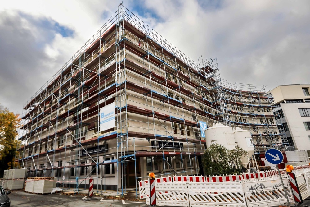 Das Wohnungsunternehmen DOGEWO21 führt aktuell eine aufwendige energetische Sanierung am Häuserriegel Löwenstr.15-17 und Küpferstr. 1 in der Innenstadt durch. Die Gebäude im 70er-Jahre-Stil erhalten eine hochmoderne, energieeffiziente Fassade mit neuen Fenstern und Fassadendämmung, so dass die Mieter*innen Heizkosten und CO2 einsparen können. Die alte Dampf-Heizanlage wird zudem von DEW21 gegen eine neue Fernwärmeanlage ausgetauscht. Das rund 600 m2 große Hauptdach, ein Flachdach, wird komplett erneuert und mit erhöhter Wärmedämmung versehen. Das 300 m2 große Dach der Werkstätten im Innenhof wird außerdem vollständig begrünt. Zusätzlich werden die Terrassen und Balkone verlängert und bekommen Glasbrüstungen. Laubengänge, Vordächer und die Treppenhäuser werden ebenfalls saniert. Auch die Haustüren werden ausgetauscht und für mehr Komfort und Sicherheit erhalten die Mieter*innen neue Gegensprechanlagen. Abgerundet wird die Maßnahme durch eine neue Farbgebung der bisher eher dunklen Fassade: der neue Anstrich erfolgt in samtweiß mit Grüntönen, zusätzlich wird die Fassade mit beleuchteten Glaselementen versehen. Auf Ebene der Ladenlokale im Erdgeschoss werden die Häuser mit modernem, grauem Klinker versehen und die z. T. verbauten Glasbausteine weichen bodentiefen Fenstern. DOGEWO21 plant die Fertigstellung der knapp 1,5 Mio. Euro teuren Baumaßnahme für Sommer 2022. Info: Mit über 16.300 Wohnungen zählt DOGEWO21 zu den größten Vermietern in Dortmund. 2021 investiert das Unternehmen rund 34,5 Millionen Euro in Neubauprojekte, Modernisierung und Instandhaltung.