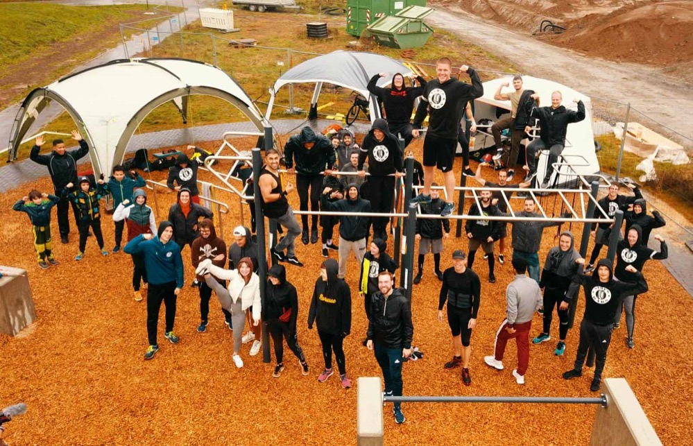 Erfolgreicher Vereins Kick Off mit mehr als 40 Teilnehmenden trotz Starkregen im neuen Sport- und Freizeitpark in Dortmund Hombruch Während manch einer den verregneten Sonntag lieber in den eigenen vier Wänden verbrachte, zeigte sich am neuen Sport- und Freizeitpark in Dortmund Hombruch trotz der Wetterbedingungen ein erstaunliches Bild. Mehr als 40 Teilnehmende kamen zum Vereins Kick Off des neu gegründeten Vereins „SchubBars – Calisthenics Dortmund e.V.“, um an der öffentlichen Calisthenics Anlage eine gemeinsame Trainingseinheit zu absolvieren. Bereits aus der Entfernung fiel das Geschehen an der Jugendfreizeitstätte in Hombruch ins Auge, denn nicht nur die motivierenden Zurufe der zahlreich Erschienenen, sondern auch spektakuläre Schwünge und Handstände erregten Aufmerksamkeit. Calisthenics heißt der neue Trend aus den USA, der verstärkt auch Einzug in die deutschen Städte nimmt. Das Training mit dem eigenen Körpergewicht vereint Elemente aus dem klassischen Turnen mit bekannten Fitnessübungen und bietet so ganz neue Formen der körperlichen Betätigung. Neben Kraft, Beweglichkeit und Koordination geht es beim Calisthenics um das soziale Miteinander, denn trainiert wird gemeinsam in der Gruppe.  „Mit den SchuBars haben wir eine Calisthenics Anlaufstelle für alle Interessierten in Dortmund gegründet. Wir leben die Gemeinschaft, motivieren uns gegenseitig und schaffen ein Umfeld, in dem jeder unabhängig der Vorerfahrungen seine individuellen Grenzen erfahren und über sich hinauswachsen kann“, erzählt Björn Karweger, Vorsitzender des Vereins, voller Freude über die zahlreiche Beteiligung am Kick Off. Der Vereinsname SchubBars setzt sich aus den Wörtern „Schub“, dem Motivationsruf des Vereins und „Bars“, zu deutsch Stangen, an denen trainiert wird, zusammen. Fortan bieten die SchubBars wöchentliche sowohl angeleitetes, als auch freies Training an, zu dem alle Interessierten eingeladen sind. David Gwizdz, Präsident des Deutschen Calisthenics und Streetlifting Verband e.V., der aus Gütersloh zum Kick Off anreiste, lobte die Entwicklungen in Dortmund: „Multifunktionale Bewegungsräume mit integrierten Calisthenics Anlagen sind ein attraktiver Ort, um Jugendliche für Bewegung und Sport zu motivieren. Mit einem gut vernetzen Verein in Dortmund erschließt sich das Potenzial, nachhaltige und niedrigschwellige Angebote im Bereich der Kinder- und Jugendförderung aufzubauen.“ Während der Wintermonate hoffen die SchubBars nun auf geeignete Trainingsmöglichkeiten in den Dortmunder Sporthallen. Nicht nur deshalb hat sich der Verein dem Stadtsportbund Dortmund e.V. angeschlossen. „Wir setzen uns dafür ein, dass sich möglichst viele Dortmunder*innen im nahen Wohnumfeld an Calisthenics Anlagen sportlich betätigen können und möchten Alternativen zum klassischen Fitnessstudio schaffen. Daher beteiligen wir uns aktiv an der Dortmunder Sportentwicklung und stehen im Austausch mit der Politik und der Verwaltung“, so Karweger, der sich auch für die Unterstützung des Kick Offs durch das Büro für Kinder- und Jugendinteressen des Jugendamts Dortmund bedankt. Mit Blick auf die Zukunft haben die SchubBars bereits weitere Pläne. Bedingt durch die Auswirkungen der Pandemie fällt es vielen Jugendlichen schwer, sich aufzuraffen. Daher plant der Verein Kooperationen mit Schulen, Jugendfreizeiteinrichtungen und sozialen Trägern, um Jugendliche an ihren Lebensmittelpunkten zu erreichen, und möchte so zu einem aktiven und gesundheitsbewussten Lebensstil beitragen. „Dortmund bietet zahlreiche Perspektiven für neue Sport- und Bewegungsangebote in den Stadtteilen. Wir möchten mit unseren Angeboten einen Beitrag zur Förderung der Jugend und Stärkung der Nachbarschaft leisten“, zeigt sich Karweger optimistisch.