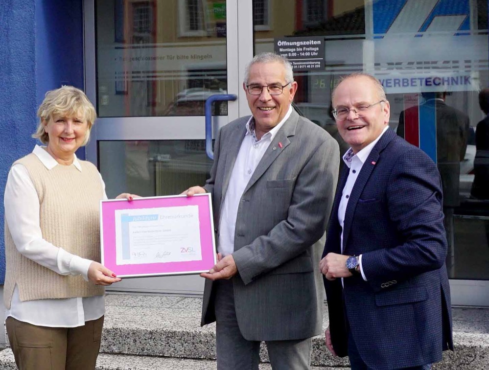 Bellen Werbetechnik GmbH aus Dortmund Schüren ist seit drei Generationen im Schilder- und Lichtreklameherstellerhandwerk erfolgreich / Stellvertretende Obermeisterin und Geschäftsführer der Schilder- und Lichtreklamehersteller-Innung für die Regierungsbezirke Arnsberg und Münster überreichen Urkunde zum Jubiläum Es ist ein außergewöhnliches Jubiläum: Auf 100 Jahre im Schilder- und Lichtreklameherstellerhandwerk kann die Schürener Firma Bellen Werbetechnik GmbH zurückblicken. Anlässlich des Jubiläums überbrachte Martina Gralki-Brosch, stellvertretende Obermeisterin der Schilder- und Lichtreklamehersteller-Innung für die Regierungsbezirke Arnsberg und Münster zusammen mit Geschäftsführer Ludgerus Niklas die Glückwünsche des Handwerks und überreichte eine Ehrenurkunde an Geschäftsführer Klaus Bellen. „Unsere Branche hat in den vergangenen 100 Jahren viele Trends und Umbrüche erlebt. Es verdient hohe Anerkennung, wenn sich ein Unternehmen eine so lange Zeit solide am Markt behaupten kann”, so Martina Gralki-Brosch in ihrer Laudatio. „Lob und Anerkennung verdient auch die gleichzeitig 100-jährige Mitgliedschaft in unserer Innung. Zu diesem Doppel- Jubiläum überbringen wir von allen Innungsmitglieder die besten Glückwünsche für viele weitere erfolgreiche Jahre.” Eng mit der Entwicklung des Brauereistandorts Dortmund verbunden Die Bellen Werbetechnik GmbH war 1921 von August Lange und Willy Bellen als Schildermalerei mit Glasschleiferei an der Dortmunder Nordstraße gegründet worden. Das Unternehmen hatte sich auf Echtvergoldungen für Werbegläser spezialisiert. Damit punktete der junge Betrieb in den ersten 20 Jahren seines Bestehens insbesondere bei Dortmunder Brauereien für die das Unternehmen die Werbemittelherstellung übernahm. Dank des Erfolgs konnte es sich schon sehr früh eine eigene Druckmaschine leisten. Nach dem Krieg wechselte der Betrieb seinen Standort und zog in die Innenstadt in die Nähe der Union-Brauerei. Dort wurde auch eine Siebdruckmaschine für die Serienproduktion eingerichtet. Nach dem Tod von Mitinhaber August Lange 1952 traten dann in zweiter Generation Heinz-Wilhelm und Johannes Bellen als Mitgesellschafter das Unternehmen ein. Sie erweiterten das Unternehmen, richteten neue Büroräume ein und modernisierten nicht nur die Anlagentechnik, sondern kooperierten auch mit einem Betrieb für Kunststoffverformung. So wurde das Lieferprogramm erheblich erweitert. Hergestellt wurden jetzt auch Serientransparente aus Kunststoff, Lichtwerbeanlagen, PVC-Folien und Außenwerbungen mit einem Spezialservice für Brauereien. Mit großen Schritten in die Digitalisierung In den 1990er Jahren ging dann Klaus Bellen, geprüfter Meister und Sohn von Heinz-Wilhelm Bellen in dritter Generation in die Geschäftsführung des Betriebs. In dieser Zeit der aufkommenden Digitalisierung wuchs das Unternehmen erneut und verlegte seine Produktion nach Dortmund-Schüren, wo ein neues Betriebs- und Sozialgebäude errichtet wurde. Gleichzeitig wurden zusätzliche Fertigungsbereiche aufgebaut. Dazu gehörte eine Schlosserei (Aluminium-Transparentbau) mit entsprechendem Maschinenpark, eine Lackieranlage, die Acrylglasverarbeitung und die Verarbeitung digitaler Vorlagen mit verschiedenen Plottern und Farbdruckern. Damals beschäftigte das Unternehmen bereits zwei Meister, zwei Angestellte, 12 Facharbeiter und zwei Lehrlinge. Nach dem Tod von Heinz-Wilhelm Bellen im Jahr 1999 übernahm Klaus Bellen das Unternehmen als alleiniger Gesellschafter und führt es bis heute erfolgreich weiter. Heute bietet die Bellen Werbetechnik GmbH ein breites Spektrum von qualitativ hochwertigen Werbeanlagen an. Es reicht von der Fassadenbeschriftung über die Leuchtwerbung und LED Schriften bis hin zu Schilder- und Leitsystemen für alle Anwendungsgebiete. Dank der langjährigen Erfahrung ist das Unternehmen mit seinem geschulten Fachpersonal ein gefragter Berater für Werbeanlagen jeder Art. Gleichzeitig steht der Name Bellen für die handwerklich anspruchsvolle Wartung und Reparatur sowie die zeitgemäße Umrüstung auf LED-Technik verbunden mit einer leistungsfähigen Grafik und Design-Abteilung. Der Innung stets treu geblieben Ein ganz besonderes Verhältnis verbindet die Bellen Werbetechnik GmbH mit der Schilder- und Lichtreklamehersteller-Innung für die Regierungsbezirke Arnsberg und Münster. Denn das Unternehmen kann in seinem Jubiläumsjahr nicht nur auf eine 100-jährige Geschäftstätigkeit verweisen, sondern auch auf eine 100-jährige Mitgliedschaft in der Innung. Schon bei der Gründung des Unternehmens 1921 legten August Lange und Willy Bellen Wert darauf, in der Standesgemeinschaft des Handwerks vertreten zu sein. Damit verbunden war auch stets ein besonderes Engagement im Ehrenamt. Sowohl Willy Bellen als auch Heinz-Wilhelm Bellen waren im Vorstand der Innung aktiv. Klaus Bellen, der derzeitige Geschäftsführer der Bellen Werbetechnik GmbH war bereits 1994 im Gesellenprüfungsausschuss aktiv und wurde Delegierter der Innung beim damaligen Zentralverband Werbetechnik (ZVW). 1999 fand er erstmals seinen Platz als Beisitzer im Vorstand und wurde 2004 zum stellvertretenden Obermeister gewählt. Seit 2009 steht er nun als Obermeister an der Spitze der Innungsbetriebe der Region. Bildzeile: Gratulation zum Jubiläum mit (v. l.) stellvertretender Obermeisterin der Schilder- und Lichtreklamehersteller-Innung für die Regierungsbezirke Arnsberg und Münster Martina Gralki-Brosch, Obermeister und Betriebsinhaber Klaus Bellen und Geschäftsführer Ludgerus Niklas.