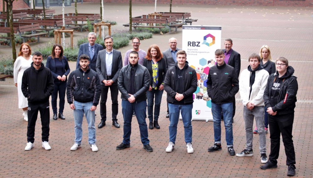 Ab Februar 2022 haben Auszubildende mit einem mittleren Schulabschluss und der Zustimmung ihres Ausbildungsbetriebes in Dortmund die Möglichkeit, gleich zwei Abschlüsse in ihrer dreijährigen Ausbildung zu erwerben: den Berufsabschluss sowie die Fachhochschulreife. Möglich macht dies das neue Bildungsangebot „Ausbildung plus FHR“ des Regionalen Bildungszentrums Dortmund, das in einem landesweiten Schulversuch entwickelt und umgesetzt wird. Das Regionale Berufsbildungszentrum Dortmund, das sich aus den acht städtischen Berufskollegs und der Stadt Dortmund als Schulträgerin zusammensetzt, entwickelt in dem Schulversuch insgesamt drei solcher Bildungsgänge. Ziel ist es, die Attraktivität der dualen Ausbildung durch den parallelen Erwerb der Fachhochschulreife zu steigern. Eine gezielte und individuelle Förderung der Schüler*innen sichert die nachhaltige Vermittlung und verbessert die Anschluss- und Integrationsperspektiven für zugewanderte Jugendliche. Der Schulversuch wird durch einen Beirat begleitet, der aus Vertretern*innen der Industrie- und Handelskammer, der Agentur für Arbeit, der Wirtschaftsförderung Dortmund, dem Lehrerrat der städtischen Berufskollegs, der Wissenschaftlichen Begleitung des landesweiten Schulversuchs sowie der Schulausschussvorsitzenden besteht. Durch die Fachexpertise und die langjährigen Erfahrungen kann der Schulversuch auf die lokalen und regionalen Belange angepasst und optimiert werden. „Bisher konnten wir die Ausbildung plus Fachhochschulreife nur in einzelnen Fachklassen des Dualen Systems anbieten. Durch den Schulversuch haben wir nun die Möglichkeit, allen Auszubildenden mit mittlerem Schulabschluss dieses Angebot zu unterbreiten“, so Andrea Schendekehl, Schulleiterin des Konrad-Klepping-Berufskollegs. Der Schulversuch des Regionalen Berufsbildungszentrums ermöglicht es, Auszubildende unterschiedlicher Ausbildungsberufe und Fachrichtungen ein gemeinsames Angebot zum Erwerb der Fachhochschulreife zu unterbreiten. Die Auszubildenden erhalten neben ihrem Berufsschulunterricht zusätzlichen Unterricht in den Fächern Deutsch/Kommunikation, Mathematik, Englisch und Naturwissenschaft. Die Vorteile dieses Bildungsganges liegen auf der Hand: Azubis können neben dem Erwerb von zwei Abschlüssen auch ihre persönlichen Entwicklungsperspektiven entfalten und die Chance auf die Übernahme von qualifizierten Aufgaben in ihrem Ausbildungsbetrieb steigern; Ausbildungsbetriebe können sich sicher sein, dass sie besonders motivierte und engagierte Auszubildende gewinnen, die ihren künftigen Fachkräftebedarf sichern werden. Stadträtin Daniela Schneckenburger als Mitinitiatorin des Dortmunder Schulversuches ist sich sicher: „Wir haben damit ein neues und noch attraktiveres Angebot geschaffen, das die Attraktivität der dualen Ausbildung steigert und einen nachhaltigen Beitrag zur Fachkräftesicherung in Dortmund und in der Region leistet“. Interessierte Schüler*innen erhalten weitere Auskünfte an ihrem Berufskolleg. Auf dem Foto (v.li., hintere Reihe): Isabella Nagel (päd. Geschäftsführerin der RBZ-Geschäftsstelle), Saziye Altundal-Köse (Vorsitzende des Schulausschusses), Ludger Dieckmann (Bezirksregierung Arnsberg), Markus Herber (Schulleiter Robert-Bosch-Berufskolleg), Dirk Engelsking (Agentur für Arbeit Dortmund), Andrea Schendekehl (Schulleiterin Konrad-Klepping-Berufskolleg), Prof. Dr. Detlef Buschfeld (Universität zu Köln – Wissenschaftliche Begleitung), Michael Ifland (IHK zu Dortmund), Wiebke Müller (Vertreterin der Lehrerräte); vordere Reihe: Schüler, die das Angebot „Ausbildung plus FHR“ nutzen werden.