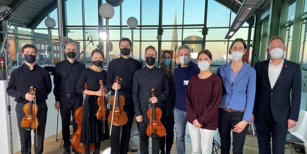 Ein ehemaliger Patient des Dortmunder Centrum für Zelltransplantation (DCZ) spielte ein Konzert im Panorama Café des St. Johannes Hospitals. Er ist ein junger Musiker, der vor 2 Jahren in der Stammzelltransplantationseinheit der Klinik für Innere Medizin II eine Blutstammzelltransplantation erhalten hat. Damit möchte er sich bei den Mitarbeitenden mit dem Weihnachtskonzert bedanken und Patienten, die in diesen Tagen im Krankenhaus sind, eine Freude machen. Für einen besonderen weihnachtlichen Moment sorgte der Dortmunder Bratschist gemeinsam mit seinen Kollegen. Bereits vor drei Jahren war er an einer Leukämie erkrankt und durchlief mehrere zunächst erfolgreiche Chemotherapien. Dennoch kam die Erkrankung zurück und am Ende blieb nur die Blutstammzelltransplantation (Knochenmarktransplantation) als einzig rettende Therapie. Bereits seit einigen Jahren wird diese komplexe Therapie in der Transplantationseinheit im St. Johannes Hospital durchgeführt. Die Mitarbeiter:innen des KMT-Teams sind mit ihm durch schwierige Zeiten gegangen und umso mehr freuen sie sich heute darüber, dass der Patient sein Leben und seine Musik zurück gewonnen hat. „Die Begleitung von Patienten über eine so lange Zeit bringt das Team auf der Station und in der Ambulanz mit den Patienten sehr nah zusammen und jeder von uns ist dankbar und tief berührt durch dieses wundervolle Geschenk zu Weihnachten“, so PD Dr. Ralf Georg Meyer, Chefarzt der Klinik und Leiter des Transplantationszentrums. Das Konzert fand im Panorama Café des St. Johannes-Hospitals statt und da aufgrund von Coronabeschränkungen kein Publikum zugelassen war, wurde es professionell mitgeschnitten. Das Konzert wird am Neujahrstag im Krankenhaus-TV für unsere Patienten und Mitarbeitenden ausgestrahlt. Für ca. 70 Minuten wird man in die Welt der klassischen Musik entführt und kann in vorweihnachtlicher Stimmung dem Krankenhausalltag eine Zeitlang entgehen. Wir bedanken uns alle sehr herzlich für dieses tolle Konzert!