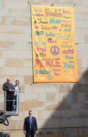 Propst Andreas Coersmeier, Thorsten Herrmann, Geschäftsführer Gemeindeverband Katholischer Kirchengemeinden Ruhr und Svenja Zahn, Dekanatsreferentin für Jugend und Familie, entrollten im Propsteihof ein großes Friedensbanner. 