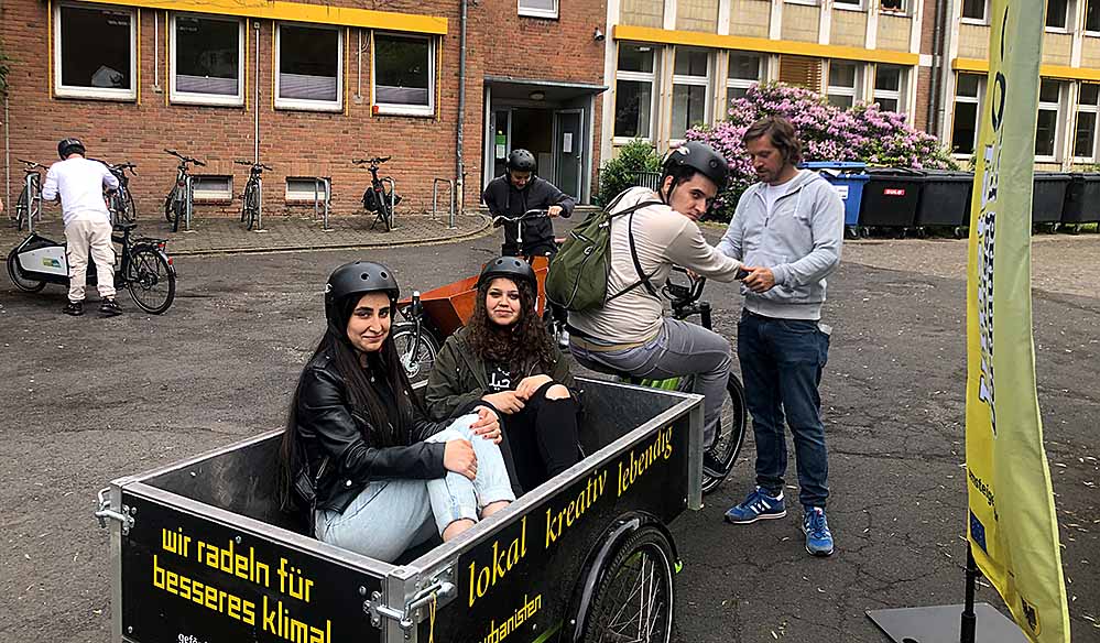 Spaß beim Lastenradfahren: Henning Boeck (rechts), Lehrer und zusammen mit dem Projekt „angekommen“ Organisator des Mobilitätstages des Robert-Schumann-Berufskollegs, gibt Schüler*innen Tipps zum Lastenradfahren.