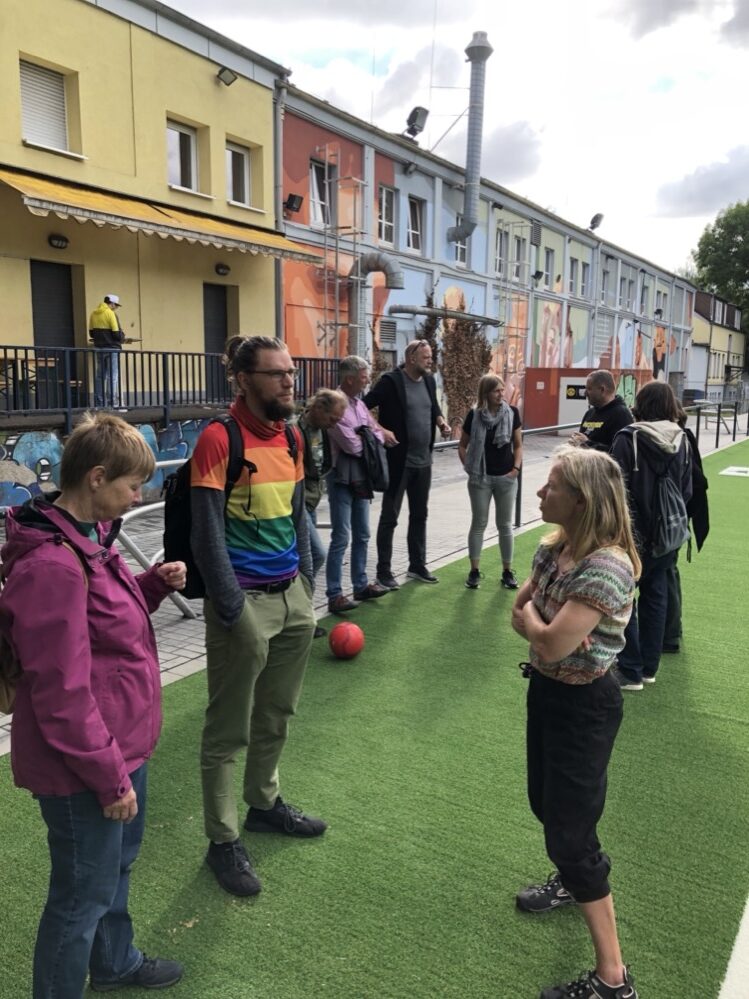 Straßenfußball und Mitternachtsturniere: GRÜNE Fraktion besucht die Nordstadtliga In der Dortmunder Nordstadtliga spielen junge Straßenfußballer*innen. Viele von ihnen sind Geflüchtete oder Kinder aus internationalen Familien. Doch ihre Herkunft spielt hier keine Rolle. Am Ende der Saison wird die Mannschaft ausgezeichnet, die am fairsten war. Im Rahmen ihrer Sommertour besuchte die GRÜNE Ratsfraktion dieses besondere Projekt aus der Nordstadt. Die Nordstadtliga ist eine über das gesamte Jahr laufende Straßenfußballliga im Dortmun-der Norden. Sie gibt es bereits seit 2001. Im Angebot der Nordstadtliga können Kinder und Jugendliche aktiv unterstützt und über den Sport in gesellschaftliche Strukturen eingebunden werden - unabhängig von ethnischer, religiöser sowie kultureller Herkunft. Hierbei sollen auch soziale Normen wie Fairness, Pünktlichkeit und Zuverlässigkeit spielerisch erlernt wer-den. Neben den Saison-Siegern erhält das Team mit den meisten Fairnesspunkten am Ende einer Saison den Fairness-Pokal. Mit den Kindern und Jugendlichen zwischen 6 bis 27 Jahren werden u.a. Streetkicks und für die Älteren sogenannte Mitternachtsturniere durchgeführt. Der Sozialpädagoge Mirza De-mirovic und sein Team betreuen derzeit etwa 27 Mannschaften mit 150 Jugendlichen, die gemeinsam und gegeneinander kicken. Durch den präventiv-sozialen Ansatz wird sozial benachteiligten Kindern und Jugendlichen ein Angebot gemacht, welches dem Spannungsfeld "Aufwachsen in unterschiedlichen kultu-rellen Kontexten mit verschiedenen Wertvorstellungen" entgegenwirken soll. Mittlerweile sind auch der Kicker, Deutschlands größtes Fußballmagazin, und der BVB auf die Nordstadtliga aufmerk-sam geworden. Gelegentlich treffen die Jugendlichen ihre großen Vorbilder vom BVB und sprechen über Respekt und Rassismus, durften mit dem Teambus des BVB fahren und zu Spielen des BVB ins Stadion. Ein neues Highlight steht auch schon fest: Der alte Ascheplatz an der Burgholzstraße wurde durch einen Kunstrasenplatz ausgetauscht. Die Kinder und Jugendlichen freuen sich schon auf die Einweihung ab August.