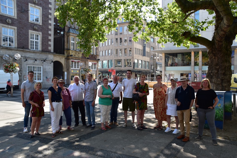 Stadtrundgang der SPD-Ratsfraktion zur Cityentwicklung Bei einem Rundgang durch die Dortmunder Innenstadt konnten sich die Mitglieder der SPD-Ratsfraktion über die Planungen der Verwaltung in der City informieren. Dabei standen insbesondere die Stadt- und Quartiersentwicklung sowie die Entwicklung des Handels auf dem Hellweg im Mittelpunkt. „Seit geraumer Zeit beschäftigt sich der Rat intensiv mit der Innenstadtentwicklung. Klar ist, dass sich die City bei den veränderten Rahmenbedingungen in den kommenden Jahren verändern wird und das auch muss. Die weitere Attraktivierung der City ist erklärtes Ziel der SPD-Fraktion. Hierzu gehört z.B. die Steigerung der Aufenthaltsqualität verbunden mit neuen Konzepten für Handel, Kultur, Gastronomie, Handwerk und Wohnen. Insgesamt sind wir positiv gestimmt und sind auf einem guten Weg, dass die Dortmunder Innenstadt auch in den kommenden Jahren attraktiv bleibt“, erklärt die Vorsitzende der SPD-Ratsfraktion Dortmund, Carla Neumann-Lieven. Wie wichtig die Klimafolgeanpassung für Dortmund und insbesondere die stark verdichtete Innenstadtlage ist, konnte bei knapp 40 Grad im Schatten sehr anschaulich besprochen und diskutiert werden. Hierbei ist es der SPD-Fraktion besonders wichtig, dass künftige Innenstadtplanungen ein deutliches Mehr an Grün vorsehen, eher auf hellere Pflasterungen und Fassaden setzen und weitere klimafreundliche Maßnahmen Berücksichtigung finden. Nur so können die Temperaturen im Innenstadtbereich bei den zu erwartenden zunehmenden Hitzeperioden insgesamt gesenkt werden. Ein Beispiel hierfür ist der temporäre Paradiesgarten auf dem Reinoldikirchplatz, der bereits das zweite Jahr in Folge einen Beitrag zur Reduzierung der Temperatur bei Hitzeperioden leistet. Um kurzfristig zu weiteren Lösungen zu kommen, hatte der Rat noch vor den Sommerferien beschlossen, dass als schnelle Übergangslösung in der Innenstadt sogenanntes mobiles Grün aufgestellt werden soll. Während des Termins wurde von der Verwaltung berichtet, dass Dortmund mit seiner City im Vergleich mit anderen Ruhrgebietsmetropolen noch immer eine gute Besucherfrequenz aufweist. In der ersten Jahreshälfte 2022 lag diese sogar höher als vor der Corona-Pandemie 2019. Das zeigt, dass Dortmund nach wie vor ein Publikumsmagnet auch für die umliegenden Regionen ist. „Neben den guten Shoppingangeboten spielt dabei sicherlich auch eine große Rolle, dass etliche Maßnahmen aus dem vom Rat beschlossenen Programm „Neue Stärke“ hier bereits zum Tragen kommen. Sei es die erweiterte Außengastronomie oder auch das interessante Freizeit- und Kulturangebot. Der SPD-Fraktion ist es wichtig, dass die Wirtschaftsförderung auf diesem Weg weitermacht und mit den Immobilienbesitzer*innen, den Händler*innen sowie weiteren City-Akteuren gute Lösungen für zeitgemäße Nutzungen und eine attraktive Innenstadt entwickelt. Unser erklärtes Ziel: Die Leerstände sowohl im Erdgeschoss wie auch in den oberen Geschossen müssen durch einen guten Nutzungs-Mix verschwinden“, erklärt die wirtschaftspolitische Sprecherin der SPD-Ratsfraktion, Silvya Ixkes-Henkemeier." Foto: Mitglieder der SPD-Ratsfraktion mit Heike Marzen (Wirtschaftsförderin) und Susanne Linnebach (Amt für Stadterneuerung) (beide links im Bild)