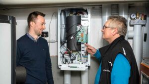 Vonovia Projektleiter Patrick Knieps (links) und Heiko Scharf, Heizungs-/Sanitärinstallateur bei Vonovia, neben der neuen Wärmepumpen-Heizungszentrale eines Mehrfamilienhauses in Dortmund.