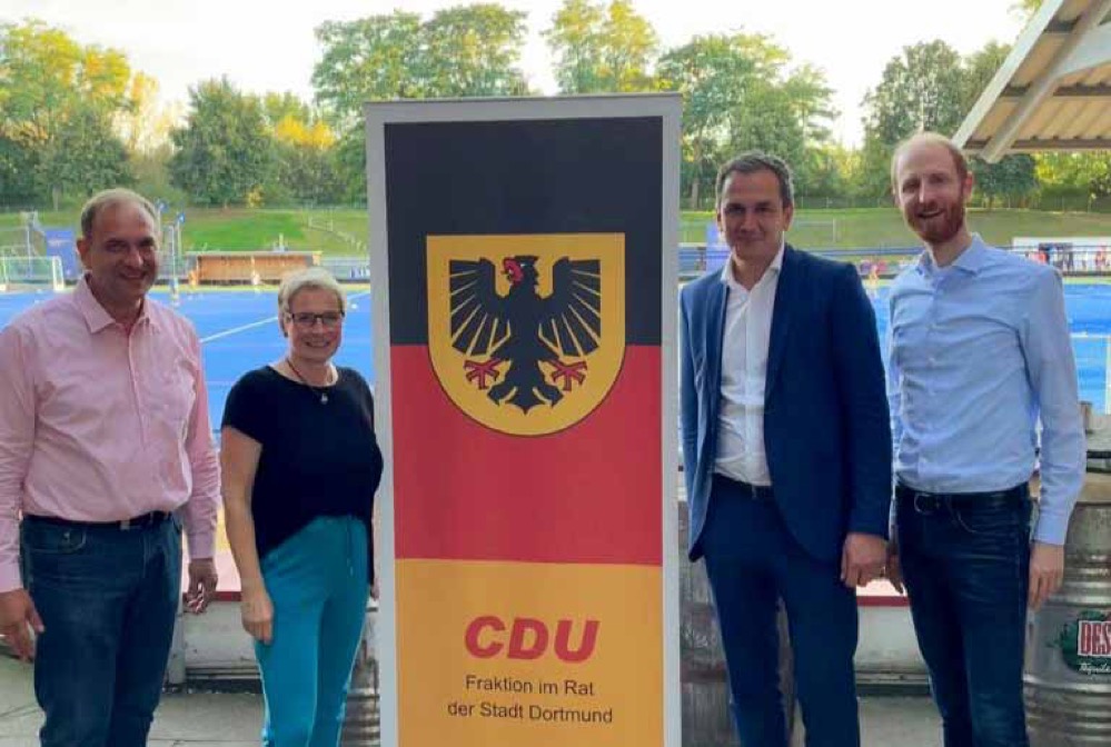Gruppenbild mit zwei Personen links und zwei rechts neben einem Plakat mit den Farben der Deutschlandflagge und dem Reichsadler, bedruckt mit "CDU, Fraktion im Rat der Stadt Dortmund"