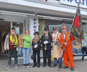 Vor der Markt-Apotheke in Huckarde machen ehemalige Bergleute, der Vorsitzende der IGBCE und die Inhaberin der Apotheke auf das Grubenunglück von 1979 aufmerksam