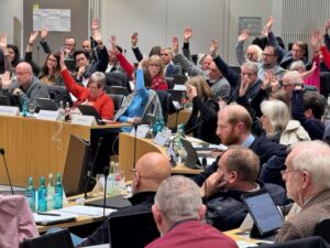 Das Foto zeigt den Sitzungssaal des Dortmunder Rates. Ratsmitglieder sitzen an ihren Plätzen, einige heben die Hand, da gerade eine Abstimmung durchgeführt wird.