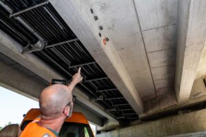 Foto des Projektingenieurs Christian Heck der auf die installierten Sensoren unter der Brücke zeigt