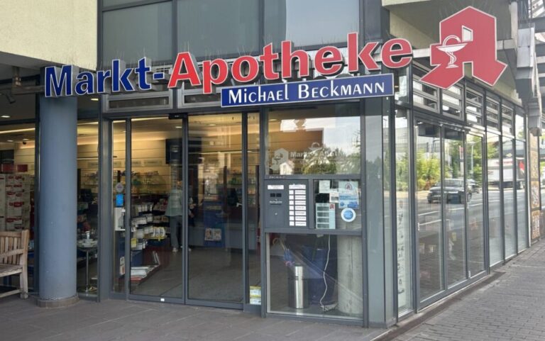 Zu sehen ist ein gläserner Eingang und ein großes Apothkene-Symbol neben dem Namen der Apotheke.