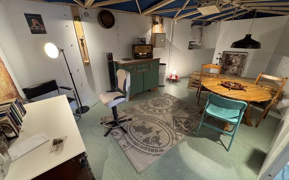 Das Foto zeigt den Escape Room, eine Schiffskabine, in dem verschiedene Möbelstücke stehen.