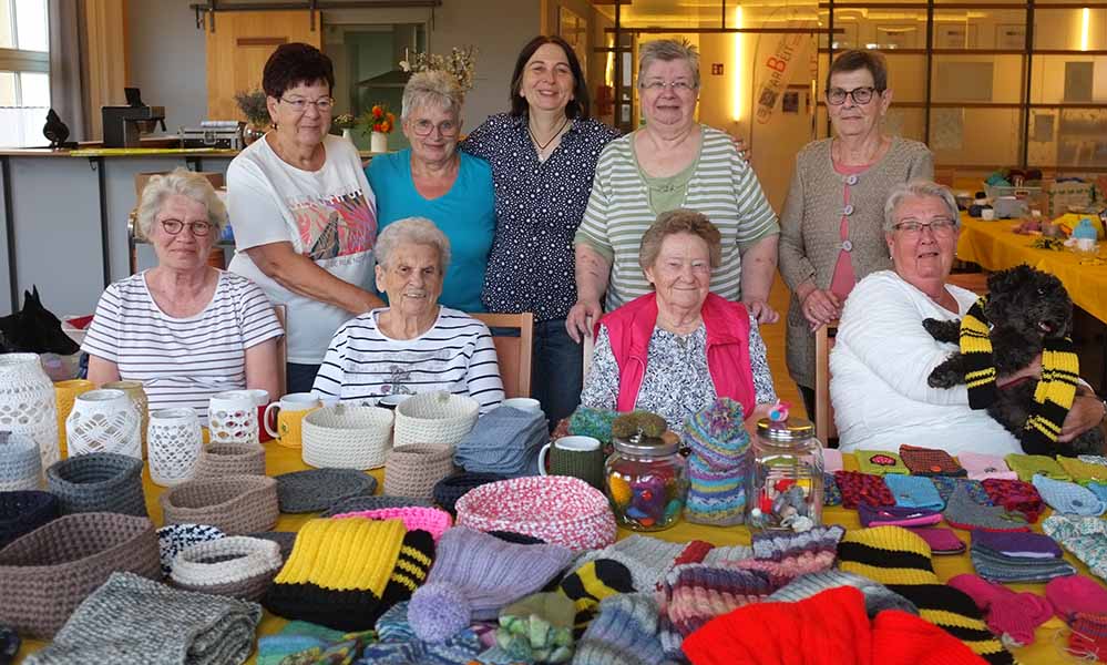 Gruppe von Frauen steht um Tisch mit selbstgemachten Strickwaren