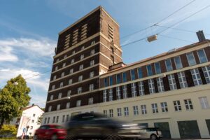 Die Straße verläuft unmittelbar vor dem Wasserturm. Das Umfeld wird durch Verkehr und städtisches Leben geprägt.