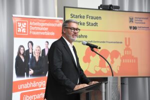 Thomas Westphal am Mikrofon. Hinter ihm zwei Aufsteller zu den Dortmunder Frauenverbänden.