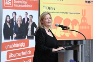 Maresa Feldmann am Mikrofon. Hinter ihr zwei Aufsteller zum Thema Frauenverbände.