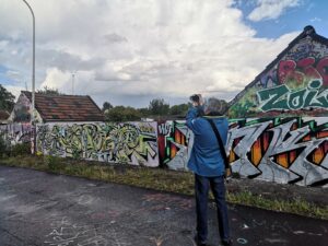Ein Mann fotografiert mit einer Kamera eine Graffitiwand