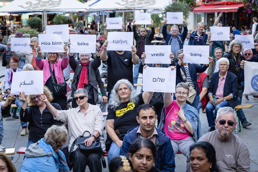 Leute halten Schilder mit "Frieden" auf verschiedenen Sprachen hoch.