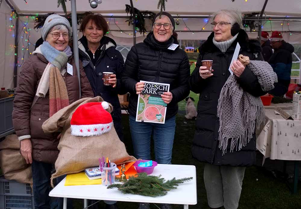 Vier Frauen stehen an einem weihnachtlich geschmückten Stand.