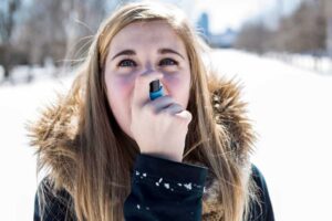 Frau benutzt Asthma Inhalator in verschneiter Landschaft