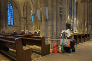 Große Kirche mit Kirchbänken. Vor den Bänken steht ein Baggy mit vielen Taschen darauf und um ihn herum.