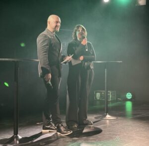 Zwei Moderatoren halten auf Bühne die Begrüßung ab.