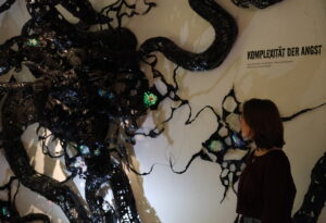 Künstlerin steht neben ihrer großen Kunstinstallation, das aus schwarzen Tentakeln besteht.