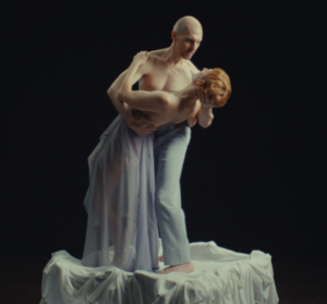 Ein Tanzpaar hält sich im Arm. Der Mann steht aufrecht, die Frau nach hinten gelehnt. Der Mann hat den Arm um den Kopf der Frau gelegt und hält sie.