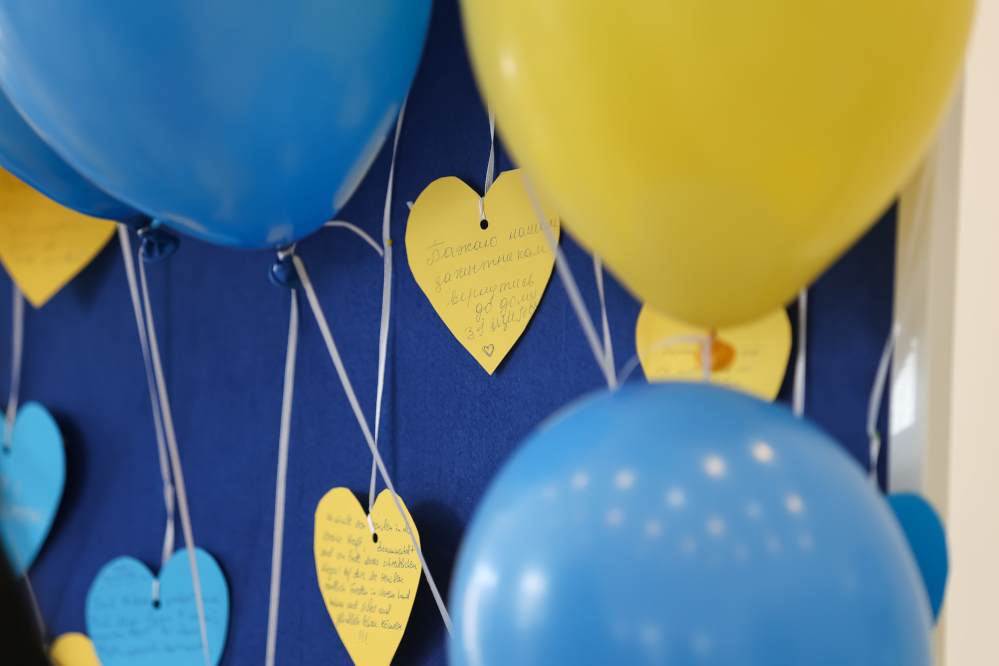 Gelbe und blaue Luftballons mit Wunschkarten an einer Pinnwand