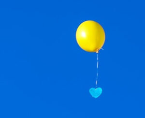 Gelber Luftballon vor blauem Himmel mit blauer herzförmiger Wunschkarte