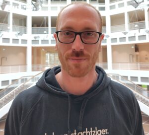 Christoph Harting schaut direkt in die Kamera. Im Hintergrund sieht man das Innere des Rathauses