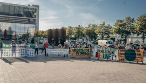 Zu sehen ist der Platz der Deutschen Einheit. In einem Halbkreis halten Menschen die Front-Banner einer Demonstration hoch.