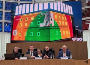 Vier Männer sitzen vor einer Leinwand auf der das Dortmunder U mit Werbung für die Olympia- und Paralympicsbewerbung beleuchtet wird.